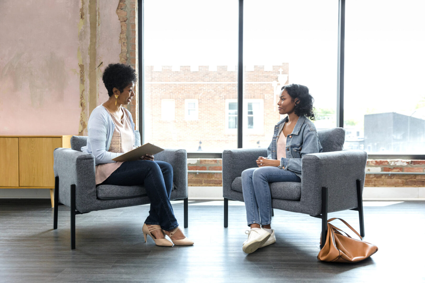 The young adult woman sits quietly with her hands in her lap as she listens to the mature adult female therapist.